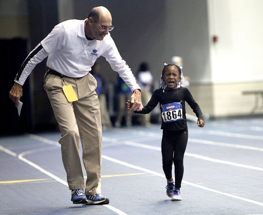 An official helps V12 Athletics runner La'Niya Fomby finish the 55 meter dash during the second day of the Jimmy Carnes Indoor Track and Field Meet at the Stephen C. O'Connell Center on Saturday, Jan. 24, 2015 in Gainesville, Fla. Fomby started to cry about half way down the track but was able to finish. (Matt Stamey/Staff photographer)